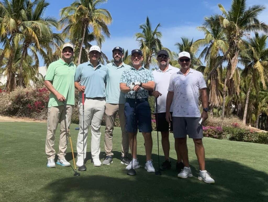 Six golfers posing together on the tee at Cabo Real Golf Club, palms behind them