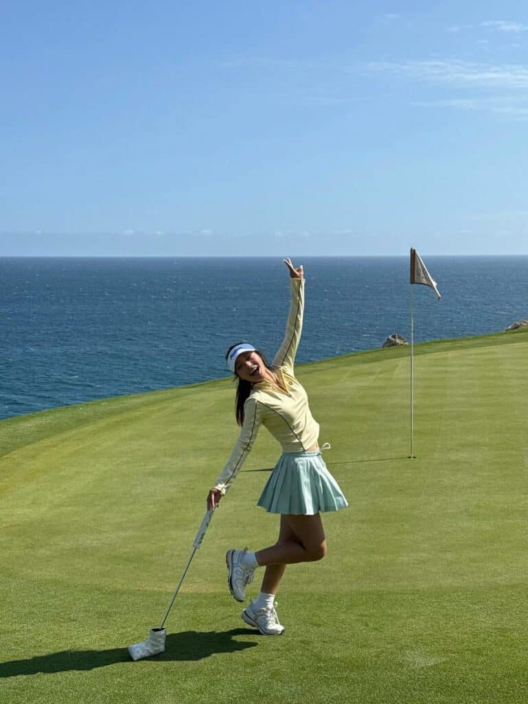A golfer raising her club after holing out on the green at Quivira Los Cabos