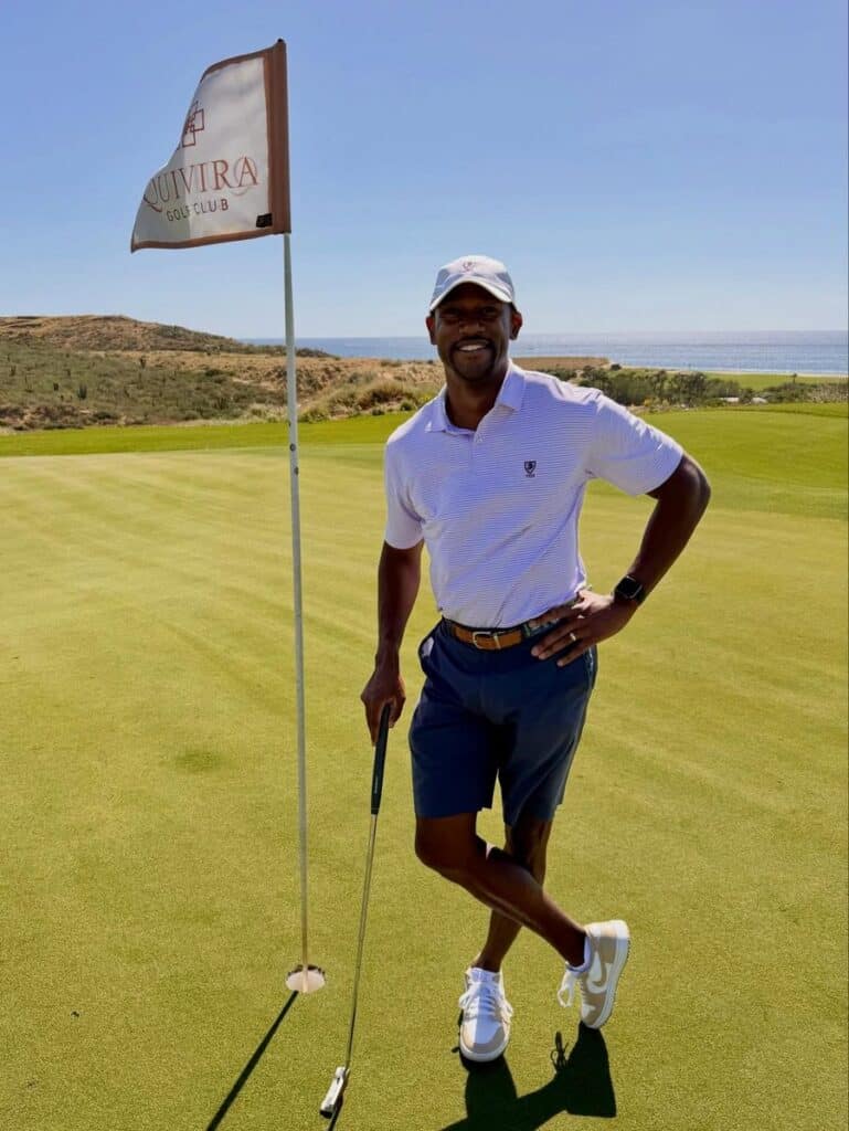 A golfer standing beside the flagstick on the green, club in hand