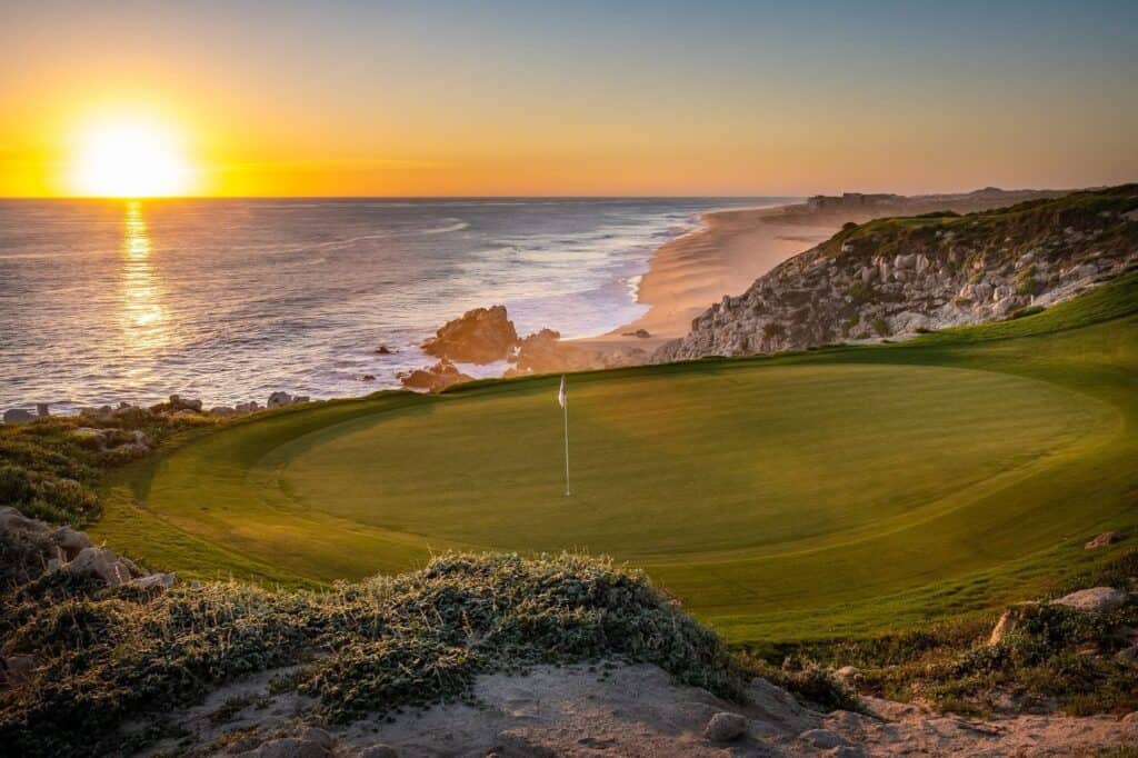The sun setting into the Pacific behind a green at Quivira Los Cabos
