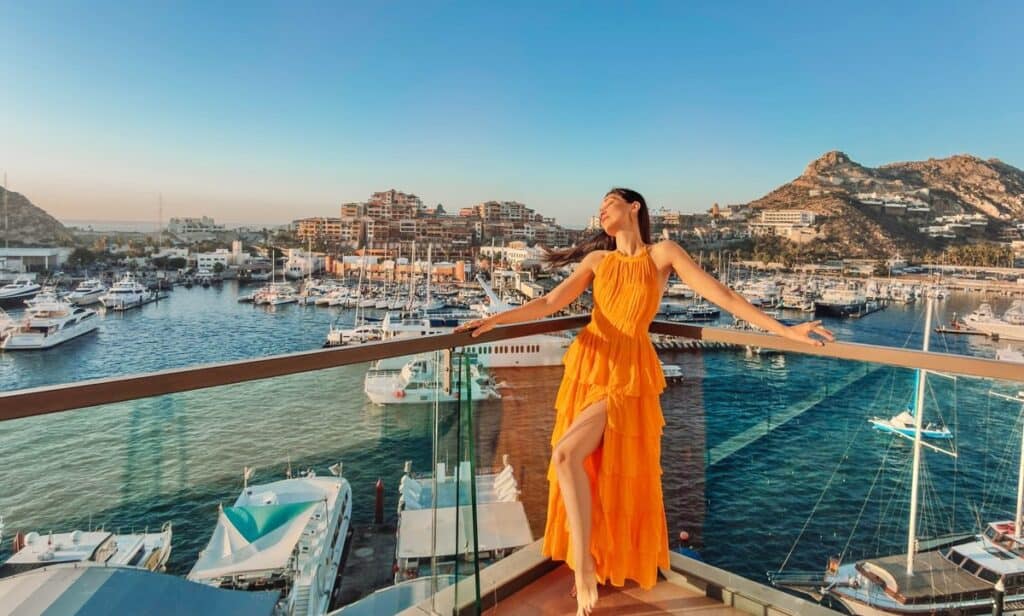 A woman in a long orange dress on a balcony above the Cabo San Lucas marina