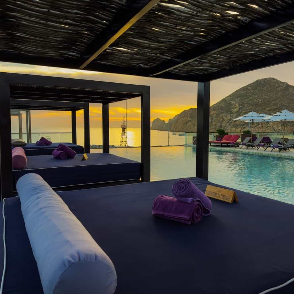 A shaded daybed facing the pool and the sea at sunrise