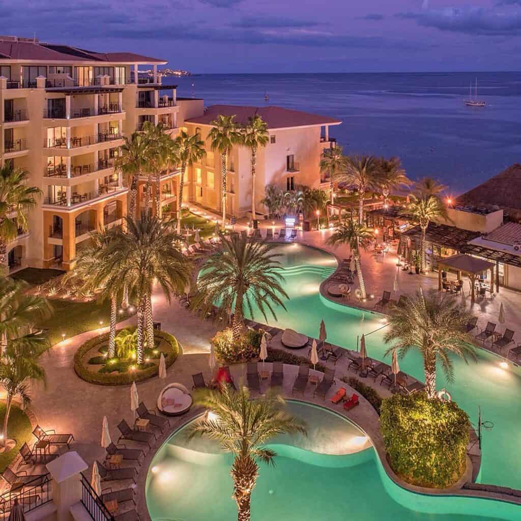 Resort pools lit at dusk above Medano Beach