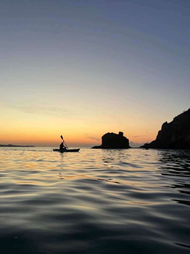 A kayaker paddling calm water along the Los Cabos coastline.