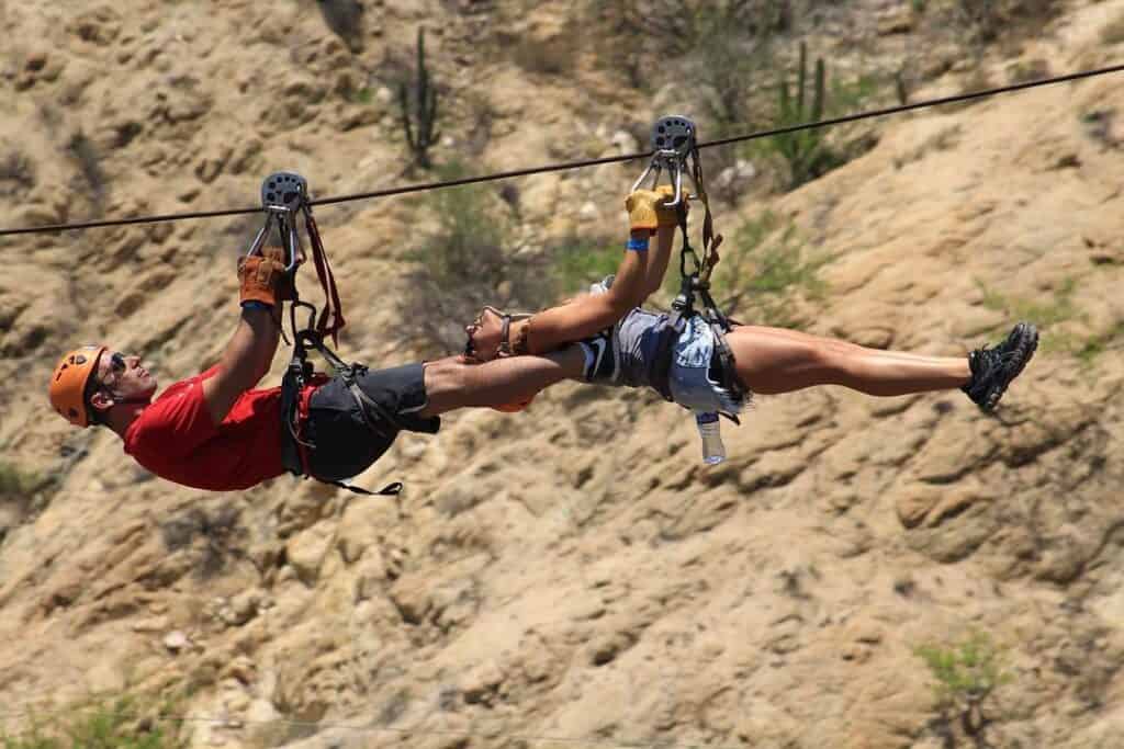 Two people ziplining side by side above a desert canyon in Los Cabos.