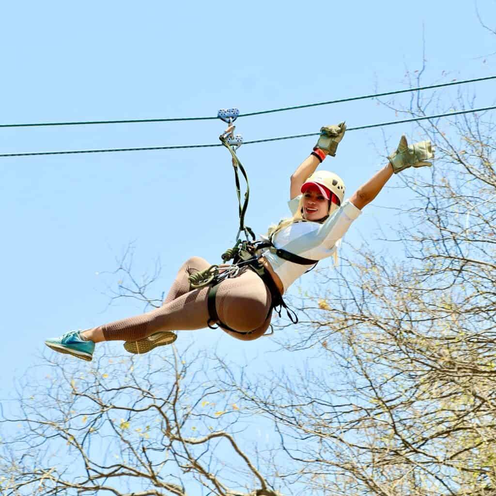 A woman ziplining with arms raised above the Los Cabos canyon.