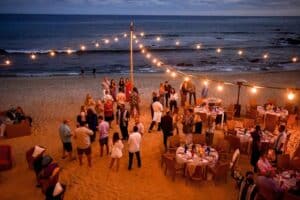 Guests at a group dinner on the sand below 7 Seas, under string lights at dusk