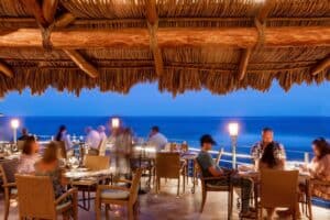 Diners under the palapa roof at 7 Seas at blue hour, with lanterns along the ocean railing