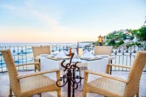 A table for four beside the wrought-iron 7 Seas sign on the terrace at dusk, with the beach and the coast behind