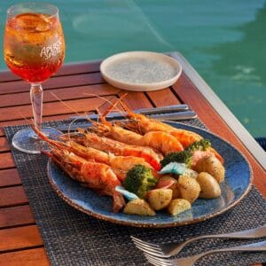 A plate of grilled prawns with baby potatoes and broccoli on a deck table above the marina water at Baja Lobster Co.