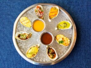 A round platter of raw and baked oysters on crushed ice with two dipping sauces at Baja Lobster Co.