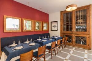 A dining area at Baja Lobster Co. with a navy banquette, wood-framed mirrors on a red wall and a wooden wine cabinet