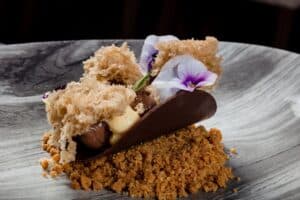 A dark chocolate taco filled with cream on a biscuit crumble, topped with crisp tuiles and viola flowers, at Café des Artistes Los Cabos