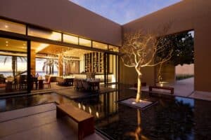 The courtyard of Café des Artistes Los Cabos at dusk, with a lit tree growing from a reflecting pool in front of the open dining room