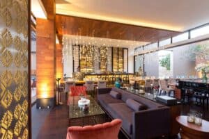 The lounge and backlit bar at Café des Artistes Los Cabos, with sofas, red velvet armchairs and a piano by the windows