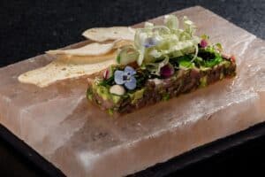 Tuna tartare with avocado served on a pink salt block with thin bread chips at Café des Artistes Los Cabos