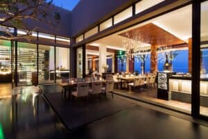 The glass wine wall and the dining room of Café des Artistes Los Cabos seen across the courtyard in the evening