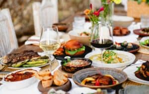 Grilled rib eye with vegetables, a burger, bread and baked dishes with glasses of white and red wine on a dinner table at Caracara