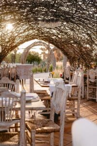 Tables under the dome of woven branches at Caracara, with a crystal chandelier overhead and the agave field beyond the arches