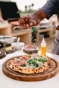 A wood-fired pizza with prosciutto and greens getting a final grating of cheese at Caracara