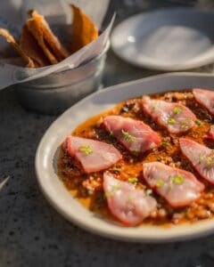 Thin slices of raw fish over a smoky red chili salsa, with a pail of tostadas on the side, at Casamarte