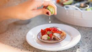 A squeeze of lime over a raw clam on the half shell, with a platter of shellfish on ice behind, at Casamarte in La Paz