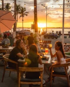 Diners on the Casamarte terrace at sunset, under string lights and palms, with the La Paz malecón and bay beyond