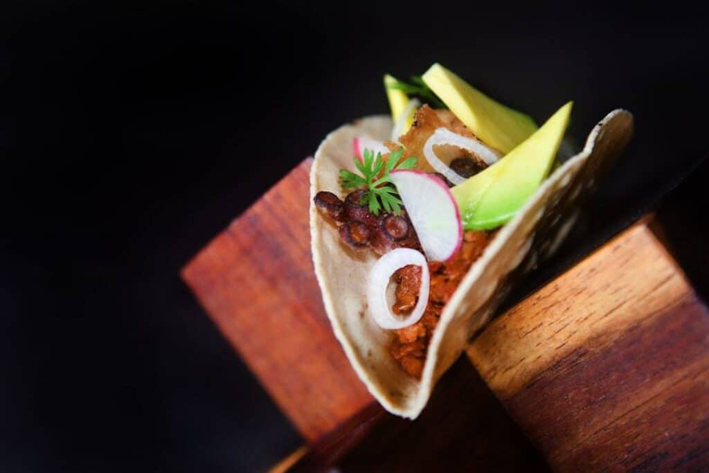 A taco with onion and avocado on a wooden stand at Frida, Grand Velas Los Cabos
