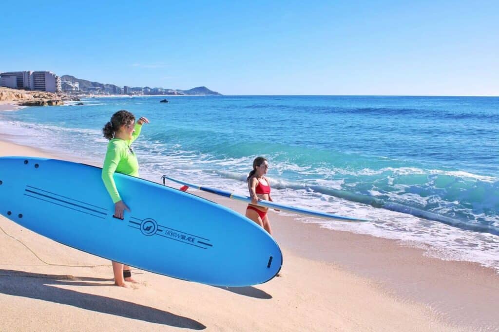 Two kids carrying a surfboard into the water at El Tule Beach