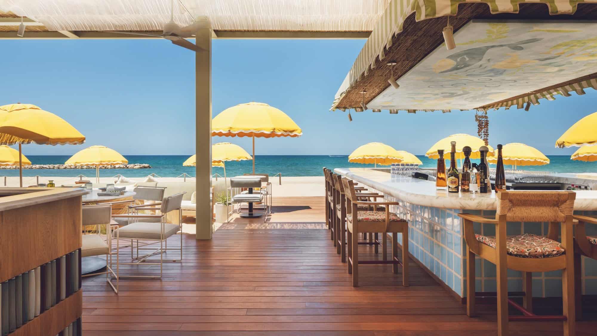 The tiled bar and shaded wooden terrace at Delphine, Costa Palmas, looking out to yellow umbrellas and the Sea of Cortez
