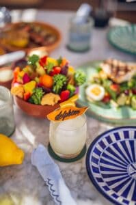 A lunch table at Delphine with a bowl of vegetable crudités, a grilled-fish Niçoise salad and a lemon drink topped with a Delphine-branded garnish