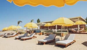 Sunbeds, lounge sofas and scalloped yellow umbrellas on the sand in front of the Delphine pavilion