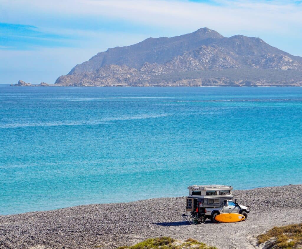 A camper van parked on the beach at Cabo Pulmo with the headland behind