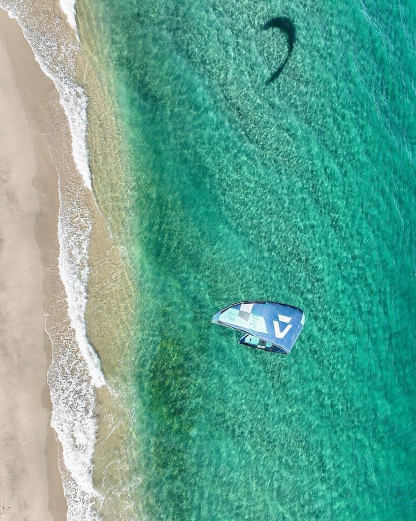 A kiteboarding kite laid on the sand beside turquoise water at Los Barriles, seen from above