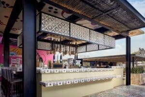 The tiled bar at El Barrio under white lattice panels, with stools along the counter and bottles on the back shelf