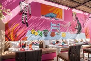 Banquette tables at El Barrio below a pink mural of a woman with a monkey, an iguana and a table set with chiles and fruit
