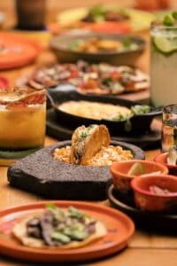 A taco set in a stone molcajete of corn kernels, with melted cheese in a cast-iron skillet, tostadas and chile-rimmed drinks at El Barrio