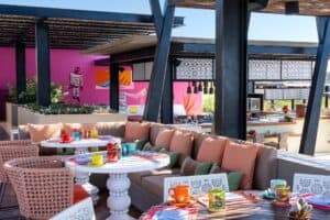 A lounge corner on the El Barrio terrace with cushioned banquettes, round white tables and bright glassware against a pink wall