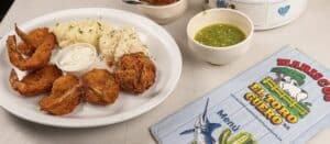Breaded shrimp with mashed potatoes, rice, tartar sauce and a cup of green salsa beside the Mariscos El Toro Güero menu