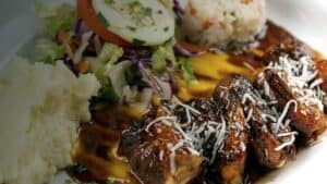 Shrimp topped with shredded coconut over a yellow sauce, with rice, mashed potatoes and salad, at Mariscos El Toro Güero