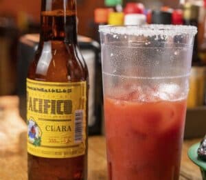 A bottle of Pacífico Clara beer next to a salt-rimmed cup of clamato over ice at Mariscos El Toro Güero