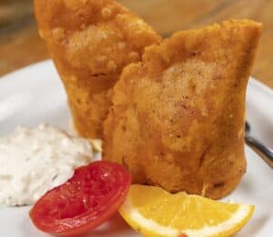 Two fried seafood empanadas with a creamy dip, a tomato slice and an orange wedge at Mariscos El Toro Güero
