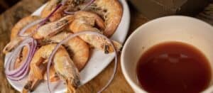 Whole cooked shrimp to peel with sliced red onion and a bowl of red sauce at Mariscos El Toro Güero