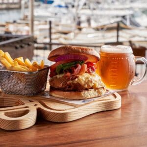 A bacon burger with fries and a draft beer in a football-style mug at Golden Legends, with the marina behind