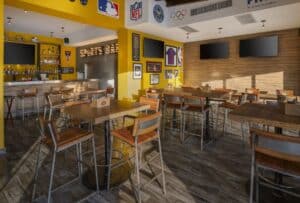 High-top tables in the Golden Legends dining room below the lit Sports Bar sign and wall-mounted screens