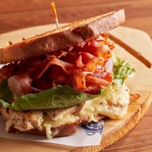 A toasted chicken and bacon sandwich on a wooden board at Golden Legends