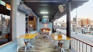Tables on the Golden Legends terrace along the marina boardwalk, with the bar's logo on the back wall