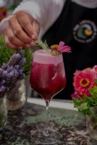A bartender at The Green Room garnishing a deep-red cocktail with fresh herbs and flowers