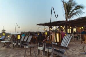 Adirondack chairs and lanterns on the sand in front of The Green Room's palapa dining area at dusk