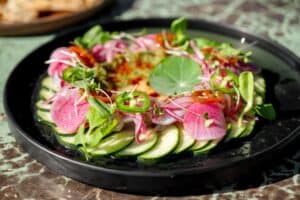 Sliced raw fish over cucumber with watermelon radish, serrano chile and a nasturtium leaf at The Green Room